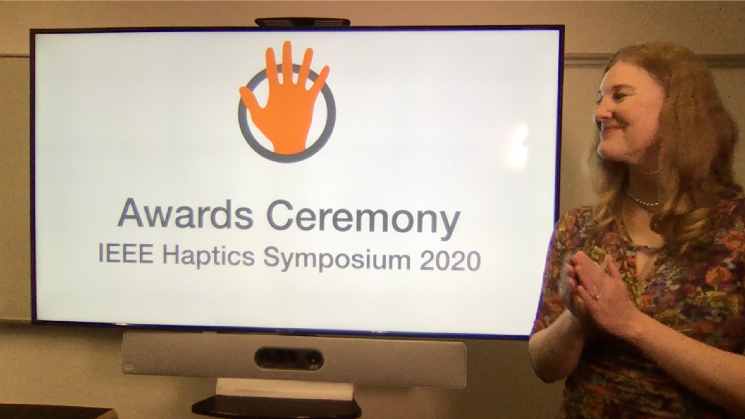 Still image from the awards ceremony with awards chair Katherine Kuchenbecker applauding all award winners